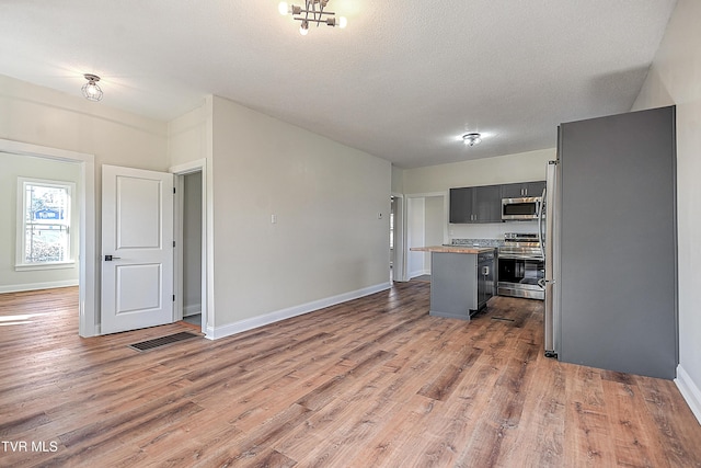 kitchen with gray cabinetry, stainless steel appliances, a center island, wood-type flooring, and a textured ceiling