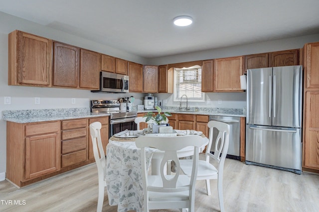 kitchen featuring stainless steel appliances, sink, light stone counters, and light hardwood / wood-style flooring