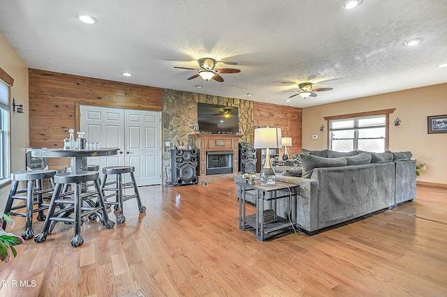 living room with ceiling fan, wooden walls, a textured ceiling, and light wood-type flooring