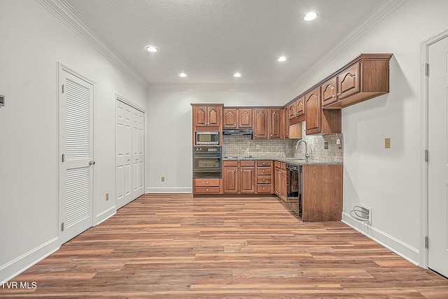 kitchen with hardwood / wood-style floors, light stone counters, ornamental molding, black appliances, and decorative backsplash