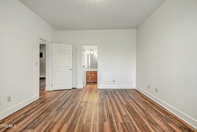 unfurnished bedroom with dark wood-type flooring, ensuite bath, and a textured ceiling