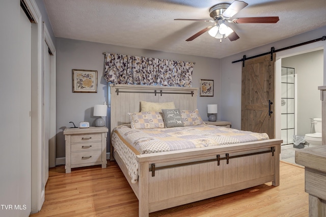 bedroom with a closet, a barn door, a textured ceiling, and light wood-type flooring