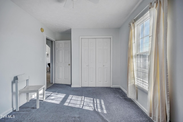 unfurnished bedroom featuring ceiling fan, dark carpet, a closet, and a textured ceiling