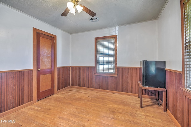 empty room with wooden walls, a textured ceiling, and light wood-type flooring