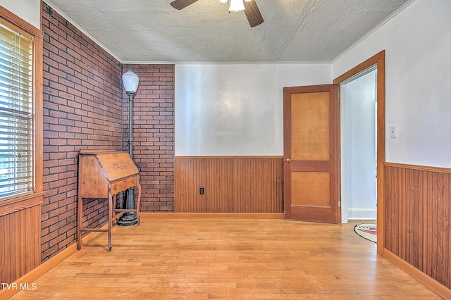 interior space featuring ceiling fan, wood walls, light hardwood / wood-style floors, a textured ceiling, and a wood stove