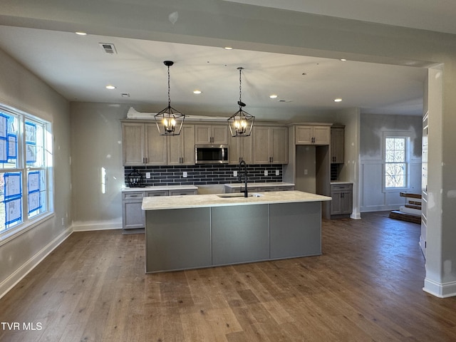 kitchen featuring hanging light fixtures, hardwood / wood-style flooring, a center island with sink, and tasteful backsplash