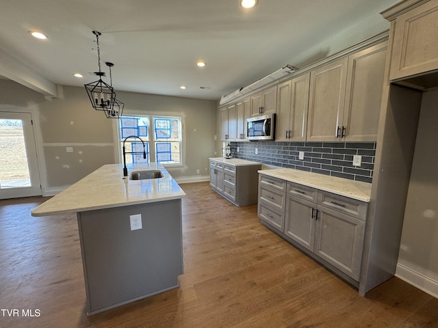 kitchen with sink, backsplash, gray cabinets, an island with sink, and hardwood / wood-style flooring