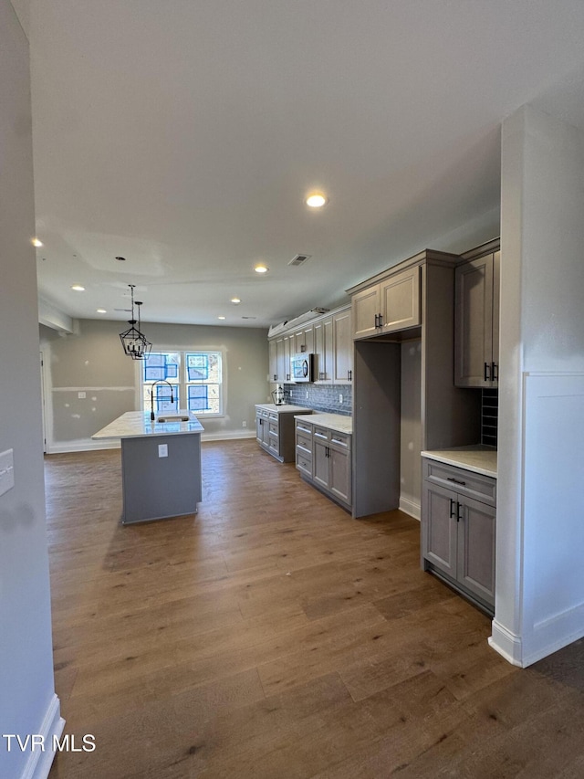 kitchen featuring a center island with sink, gray cabinetry, dark wood-type flooring, hanging light fixtures, and tasteful backsplash