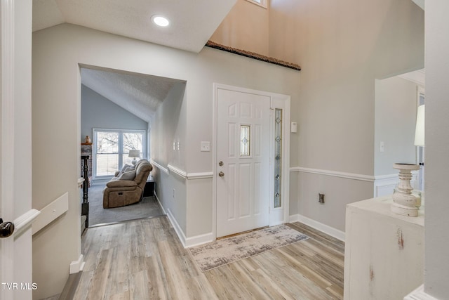 entryway featuring light hardwood / wood-style flooring, high vaulted ceiling, and a textured ceiling