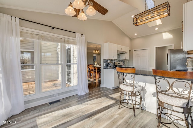 kitchen featuring lofted ceiling, crown molding, a breakfast bar area, stainless steel refrigerator, and white cabinetry