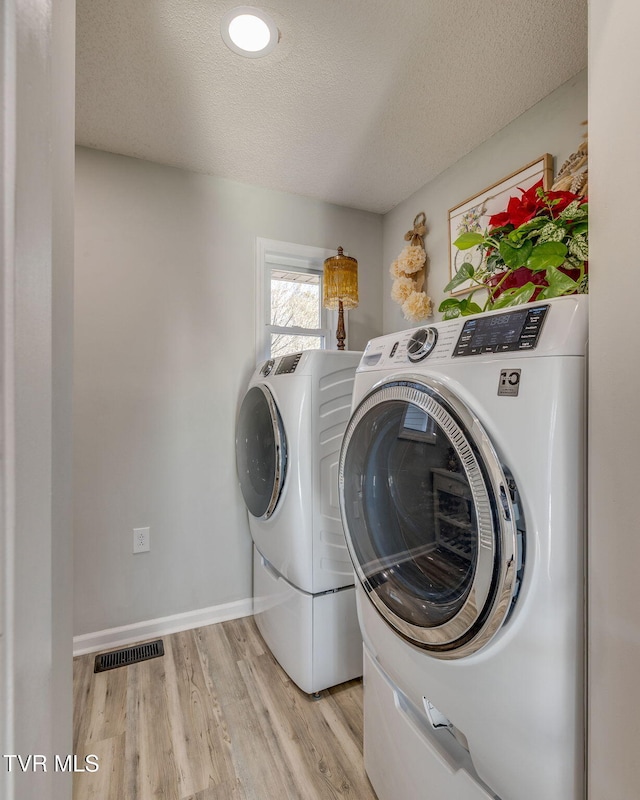 clothes washing area with washing machine and clothes dryer, light hardwood / wood-style floors, and a textured ceiling