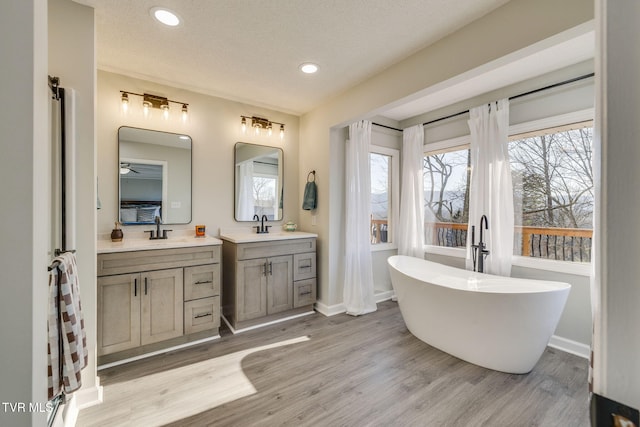 bathroom featuring wood-type flooring, vanity, a textured ceiling, and a tub to relax in