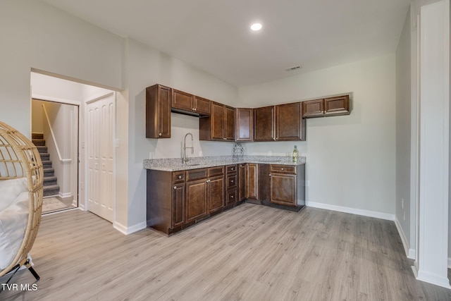 kitchen featuring dark brown cabinets, sink, light stone counters, and light hardwood / wood-style flooring