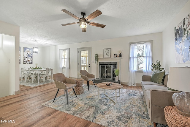 living room with a fireplace, light hardwood / wood-style flooring, a textured ceiling, and ceiling fan