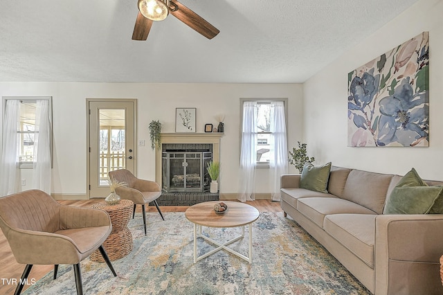 living room featuring hardwood / wood-style floors, a textured ceiling, a brick fireplace, and ceiling fan