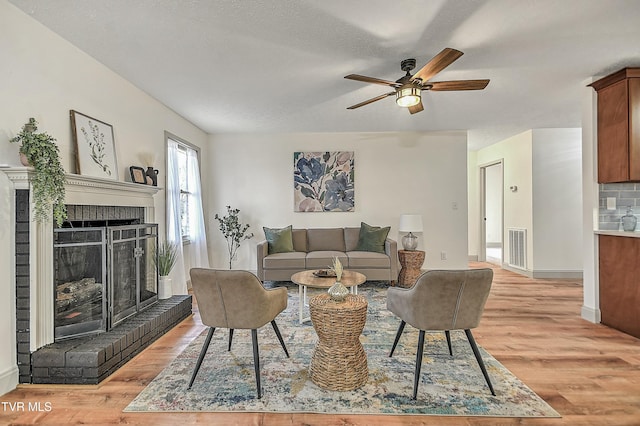 living room with ceiling fan, a textured ceiling, a brick fireplace, and light wood-type flooring