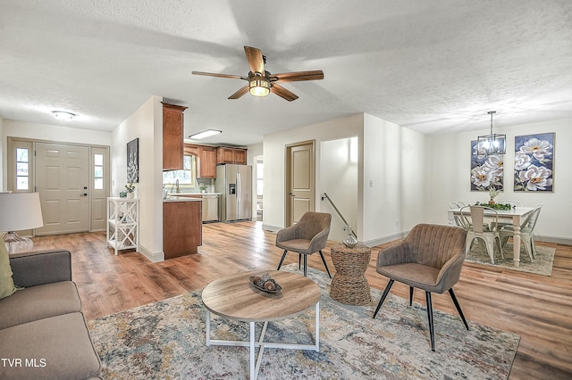 living room with ceiling fan with notable chandelier, a textured ceiling, and light wood-type flooring