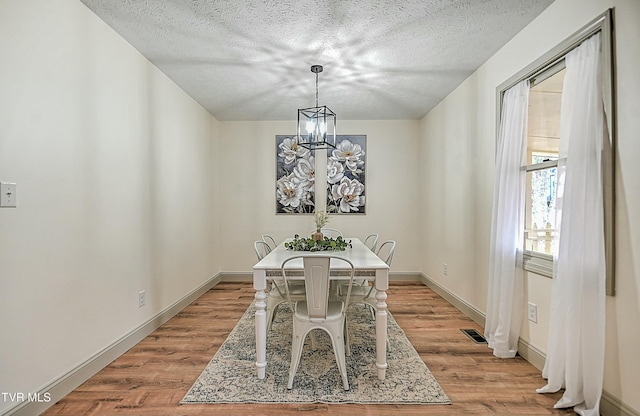 dining area featuring a chandelier, a textured ceiling, and light wood-type flooring