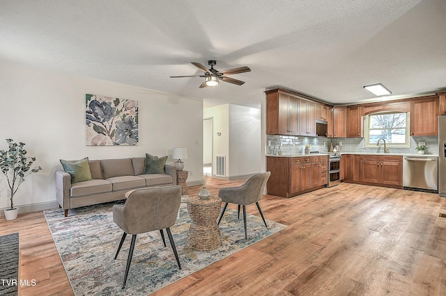 living room featuring ceiling fan, sink, a textured ceiling, and light hardwood / wood-style flooring