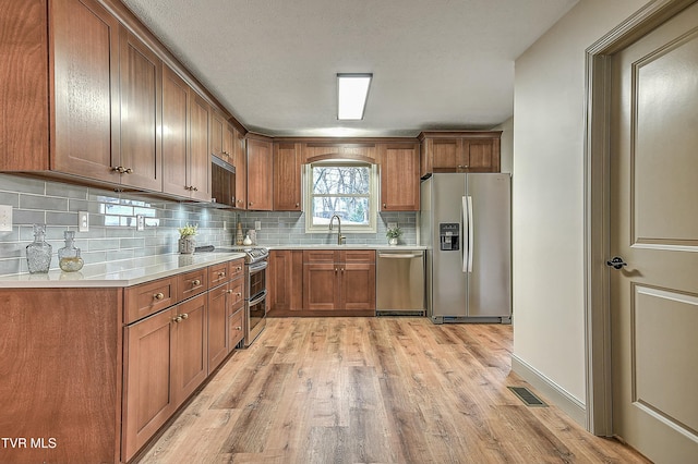 kitchen with sink, light hardwood / wood-style flooring, a textured ceiling, stainless steel appliances, and decorative backsplash