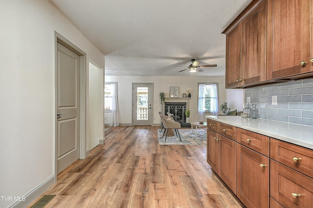 kitchen featuring ceiling fan, tasteful backsplash, a fireplace, a textured ceiling, and light wood-type flooring