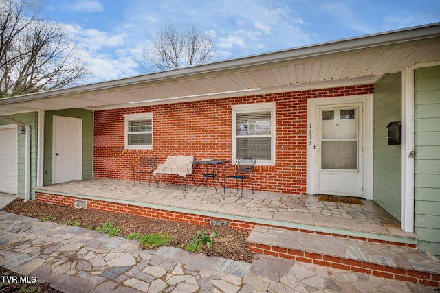 property entrance with a porch, an attached garage, and brick siding