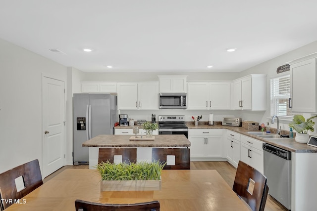 kitchen featuring a kitchen island, appliances with stainless steel finishes, sink, white cabinets, and light hardwood / wood-style floors