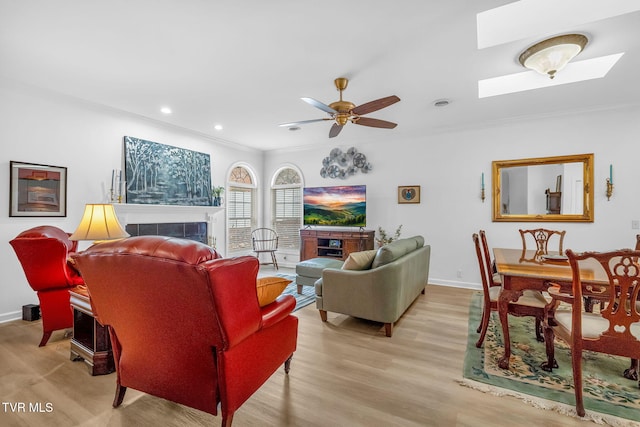 living room with a tiled fireplace, ornamental molding, ceiling fan, and light wood-type flooring