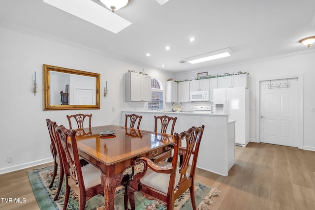 dining room featuring crown molding, a skylight, and light wood-type flooring