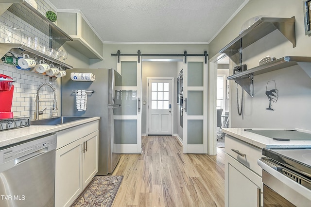 kitchen featuring sink, light hardwood / wood-style flooring, appliances with stainless steel finishes, ornamental molding, and a barn door