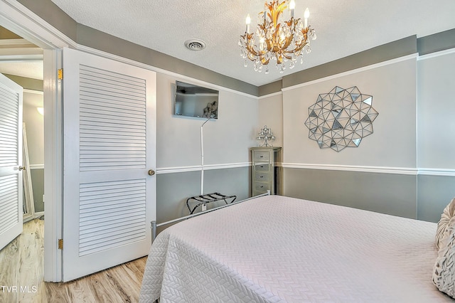 bedroom featuring wood-type flooring, an inviting chandelier, a textured ceiling, and a closet