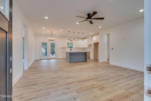 unfurnished living room featuring french doors, sink, ceiling fan with notable chandelier, and light hardwood / wood-style flooring