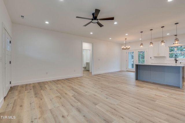 unfurnished living room featuring sink, ceiling fan with notable chandelier, and light hardwood / wood-style flooring