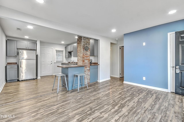 kitchen featuring stainless steel fridge, hardwood / wood-style floors, a breakfast bar area, and gray cabinetry