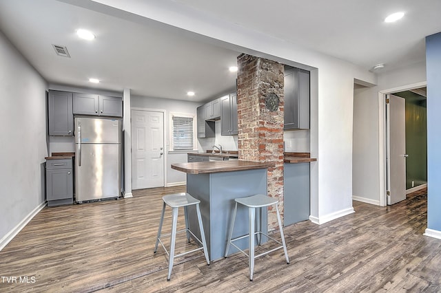 kitchen featuring dark hardwood / wood-style flooring, sink, stainless steel fridge, and a breakfast bar area