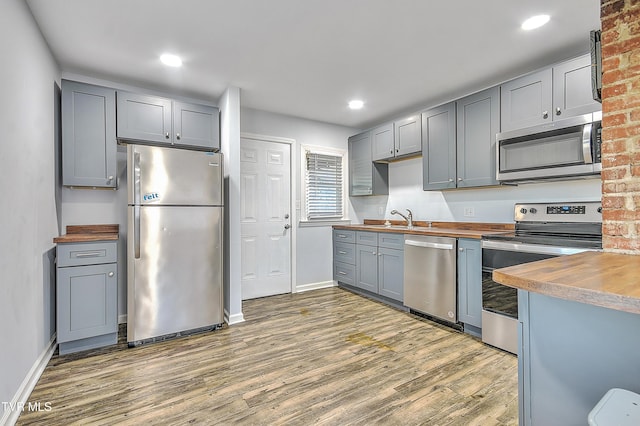 kitchen with sink, gray cabinets, appliances with stainless steel finishes, dark hardwood / wood-style floors, and wood counters