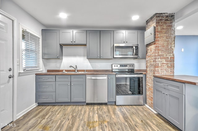 kitchen with hardwood / wood-style floors, gray cabinets, wooden counters, and appliances with stainless steel finishes