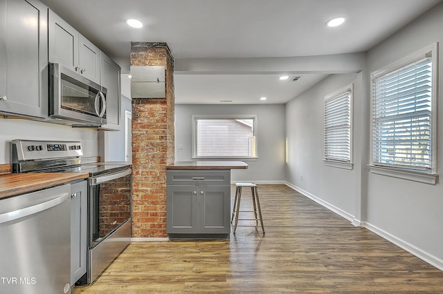 kitchen with light hardwood / wood-style flooring, gray cabinets, wooden counters, and appliances with stainless steel finishes