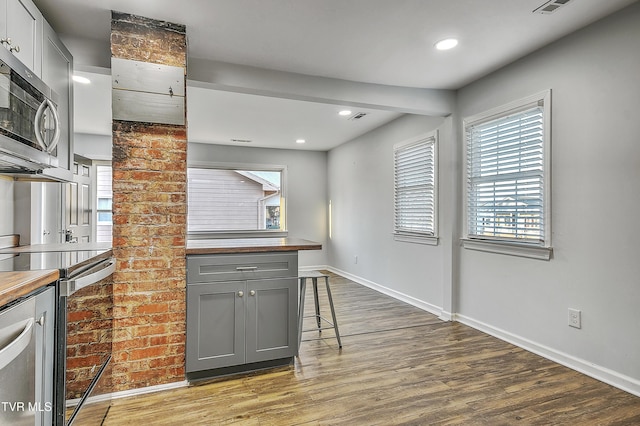 kitchen featuring wood counters, appliances with stainless steel finishes, gray cabinets, and hardwood / wood-style floors