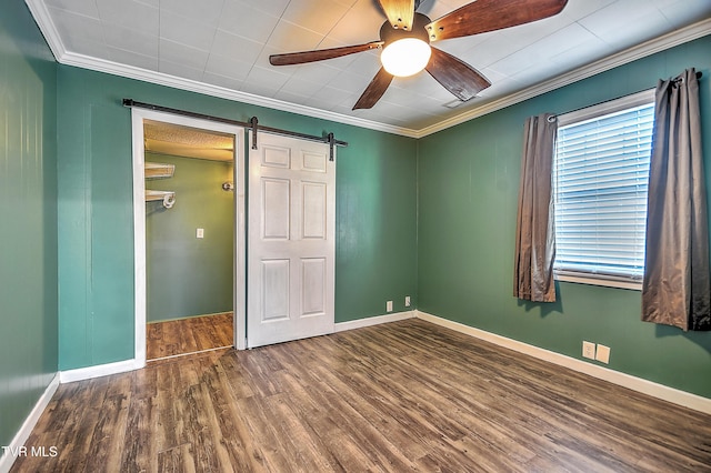 unfurnished bedroom featuring ceiling fan, dark hardwood / wood-style floors, ornamental molding, a spacious closet, and a barn door