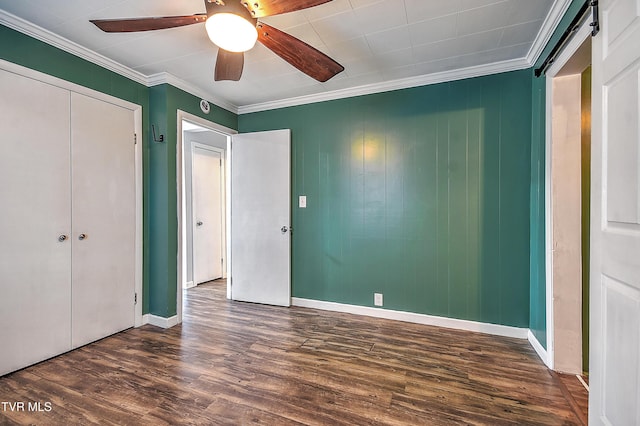 unfurnished bedroom featuring dark hardwood / wood-style flooring, ceiling fan, crown molding, a barn door, and a closet