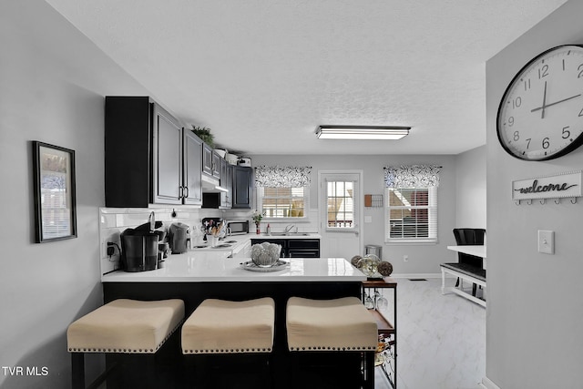 kitchen with sink, a kitchen breakfast bar, a textured ceiling, decorative backsplash, and kitchen peninsula