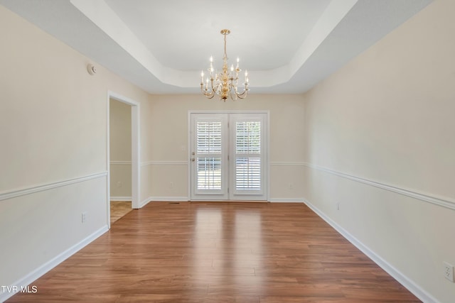 empty room with an inviting chandelier, hardwood / wood-style floors, and a tray ceiling