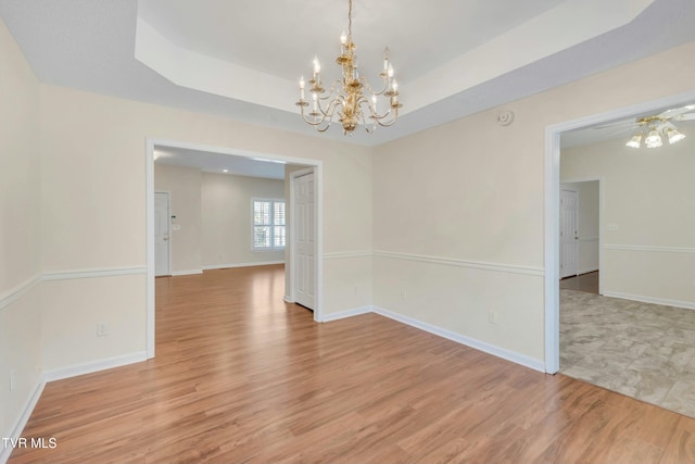 spare room with a raised ceiling, a chandelier, and light wood-type flooring