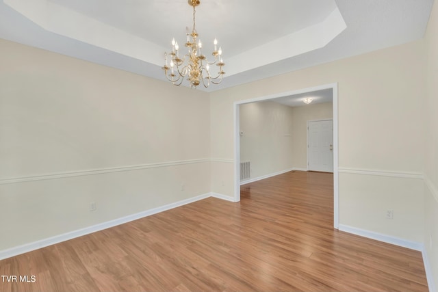 unfurnished room featuring a raised ceiling, wood-type flooring, and an inviting chandelier