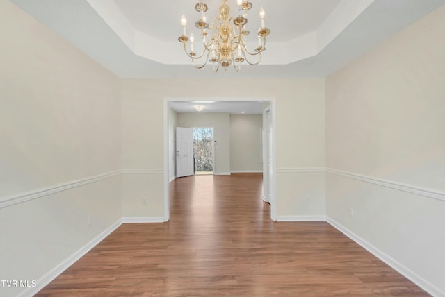 unfurnished dining area featuring hardwood / wood-style floors, a notable chandelier, and a raised ceiling