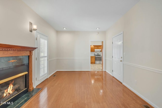 unfurnished living room featuring a tiled fireplace and light hardwood / wood-style flooring