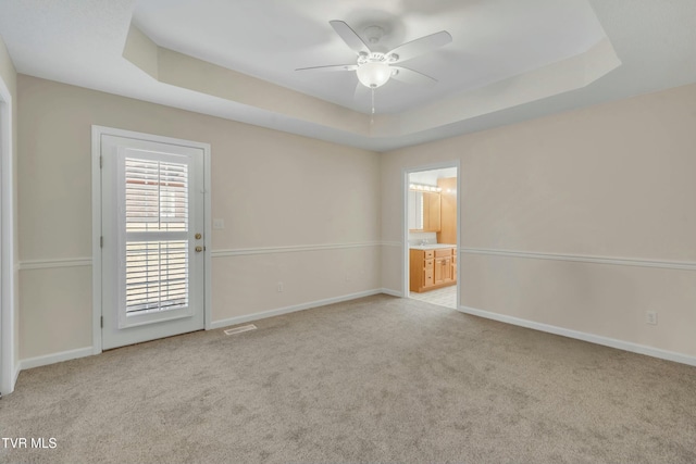 empty room with ceiling fan, a raised ceiling, and light carpet