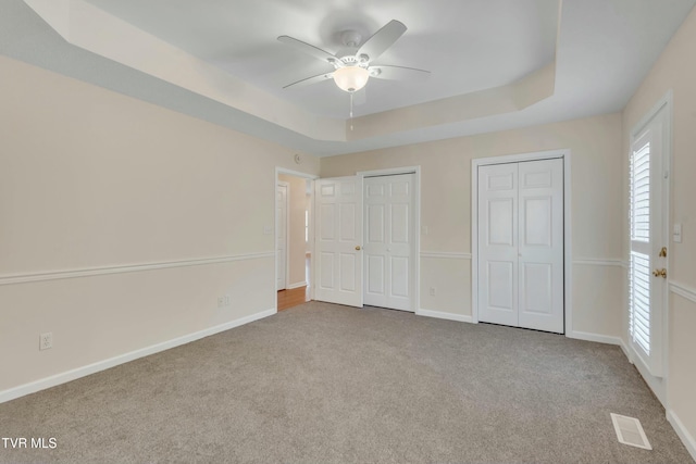 unfurnished bedroom featuring a raised ceiling, light carpet, two closets, and ceiling fan