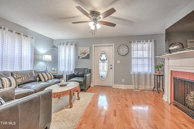 living room featuring a textured ceiling, a fireplace, ceiling fan, and light wood-type flooring